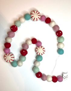 a necklace made out of felt balls and candy canes on a white background with a cat toy