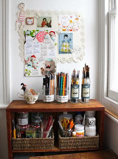 a wooden table topped with lots of crafting supplies next to a wall covered in pictures