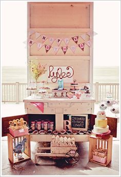 a table filled with cakes and cupcakes on top of a wooden shelf next to a window