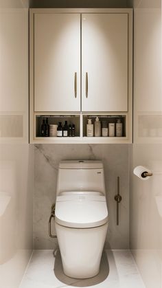 a white toilet sitting in the middle of a bathroom next to a wall mounted cabinet