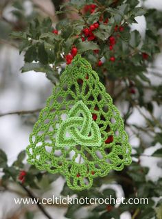 a crocheted ornament hanging from a tree branch with berries on it