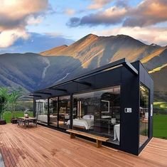 a house made out of shipping containers sitting on top of a wooden deck next to mountains