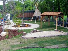 an outdoor play area with a teepee tent and sand pit in the middle, surrounded by trees