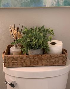 a basket with toilet paper and plants in it sitting on top of a white toilet