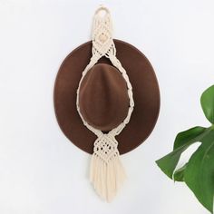 a brown hat hanging on the wall next to a potted plant with a white tassel