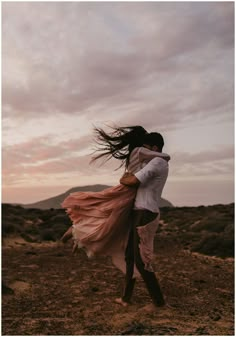 a man holding a woman in his arms while she is walking through the desert at sunset