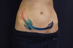 a woman's stomach with an artistic tattoo on her lower body and colorful feathers painted on it