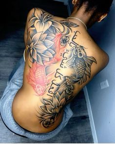 the back of a woman's body with fish and flowers tattoo on her left side