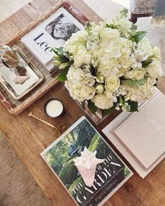 a table topped with books and flowers next to a vase filled with white hydrangeas