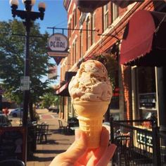 a hand holding an ice cream cone in front of a building