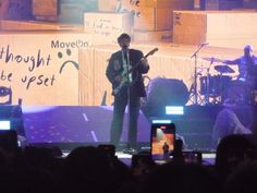 a man standing on top of a stage holding a guitar in front of an audience