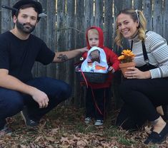 a man, woman and child sitting in front of a wooden fence with leaves on the ground