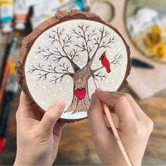 a person holding up a piece of wood with a tree and two birds painted on it