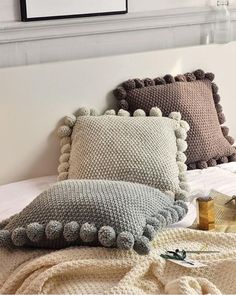 two pillows on top of a bed covered in blankets and crocheted pom - poms