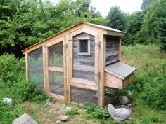 a chicken coop in the middle of a field with rocks and trees around it,