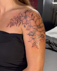 a woman wearing a black dress with flowers on her shoulder and arm tattooing it