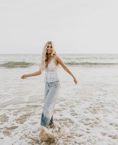 a woman is standing in the water at the beach with her arms out and smiling