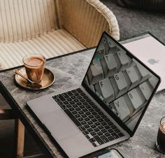 an open laptop computer sitting on top of a table next to a cup of coffee