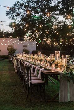 a long table set up with candles and greenery for an outdoor dinner party in the evening