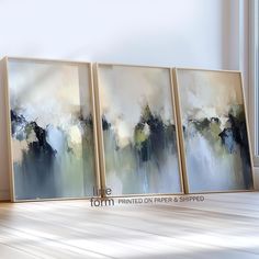 three abstract paintings are sitting on the floor in front of a window with sunlight streaming through them