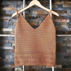 a crocheted top hanging on a wooden hanger next to a brick wall