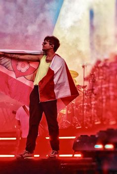 a man standing on top of a stage next to a red and white flag in front of him