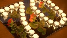 many candles are lit in front of a mirror with roses and leaves on the table