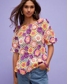 a woman wearing a crochet top with flowers on the front and side, standing in front of a purple background