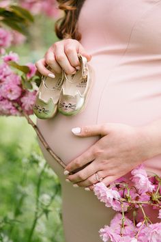 a pregnant woman holding her shoes while standing next to pink flowers