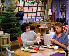 two women sitting at a table in front of a christmas tree eating cookies and drinking wine