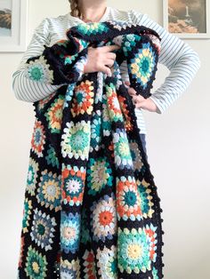 a woman is wearing a multicolored crocheted granny afghan while holding her hands on her hips