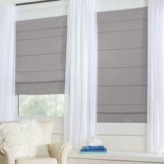 a white chair sitting in front of two windows with black shades on them and a window covering