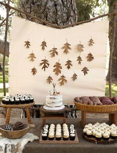 an outdoor dessert table with cupcakes, cookies and cakes in front of a tree