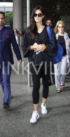 a woman walking through an airport with her headphones in her hand and other people behind her