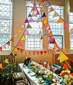 a long table is set up for a party with colorful flags hanging from the ceiling