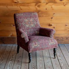 a red chair sitting on top of a wooden floor next to a wood paneled wall