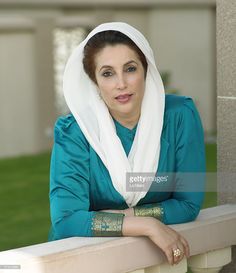 a woman wearing a headscarf leaning on a wall with her arms crossed and looking at the camera