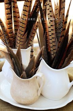 there is a white pitcher with feathers in it on the table next to another vase