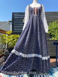 This Gunne Sax dress has a navy background with plum purple bouquets, and smaller blue/grey flowers. Trademark lace-up bodice with desert rose velvet & polka dot trim, and loopy crochet lace. Floral lace appliqué on the neckline. Long white voile sleeves with lace trimmed cuffs.  Full skirt has hip pockets & floral lace trim above ruffle hem. Dress zips up the back with waist ties.  Some things to know...this dress was hemmed up in 2 places.  I took it down to it's original length, but there is Blue Empire Waist Dress With Lace Trim, Fitted Floral Patchwork Dress For Fall, Blue Lace Trim Dress For Fall, Vintage Gunne Sax Dress, Purple Bouquets, Gunne Sax Dress, Rose Velvet, Velvet Maxi Dress, Gunne Sax