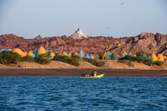 two people in a yellow boat on the water with mountains in the backgroud