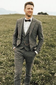 a man standing in a field wearing a suit and bow tie