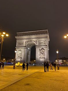 people are standing in front of the arc de trioe triumph at night with lights on