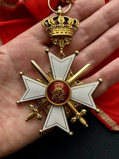 a hand holding a gold and white cross with a crown on it's head