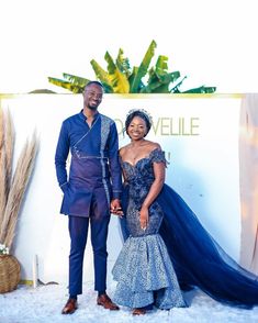 a man and woman standing next to each other in front of a white wall with plants