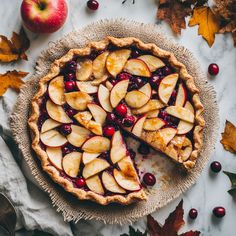 an apple pie with cranberry sauce and sliced apples on the side, surrounded by autumn leaves