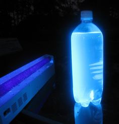 a glowing water bottle sitting on top of a table next to a blue light box