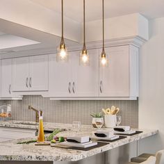 a kitchen with white cabinets and marble counter tops, lights hanging over the island area