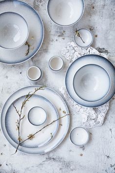 an assortment of white dishes and bowls on a gray tablecloth with twigs in the middle