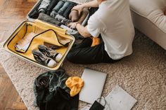 a woman sitting on the floor with an open suitcase full of clothes and shoes next to her laptop