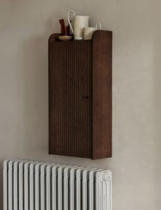 a radiator with a wooden cabinet and cups on the top, next to a wall mounted heater